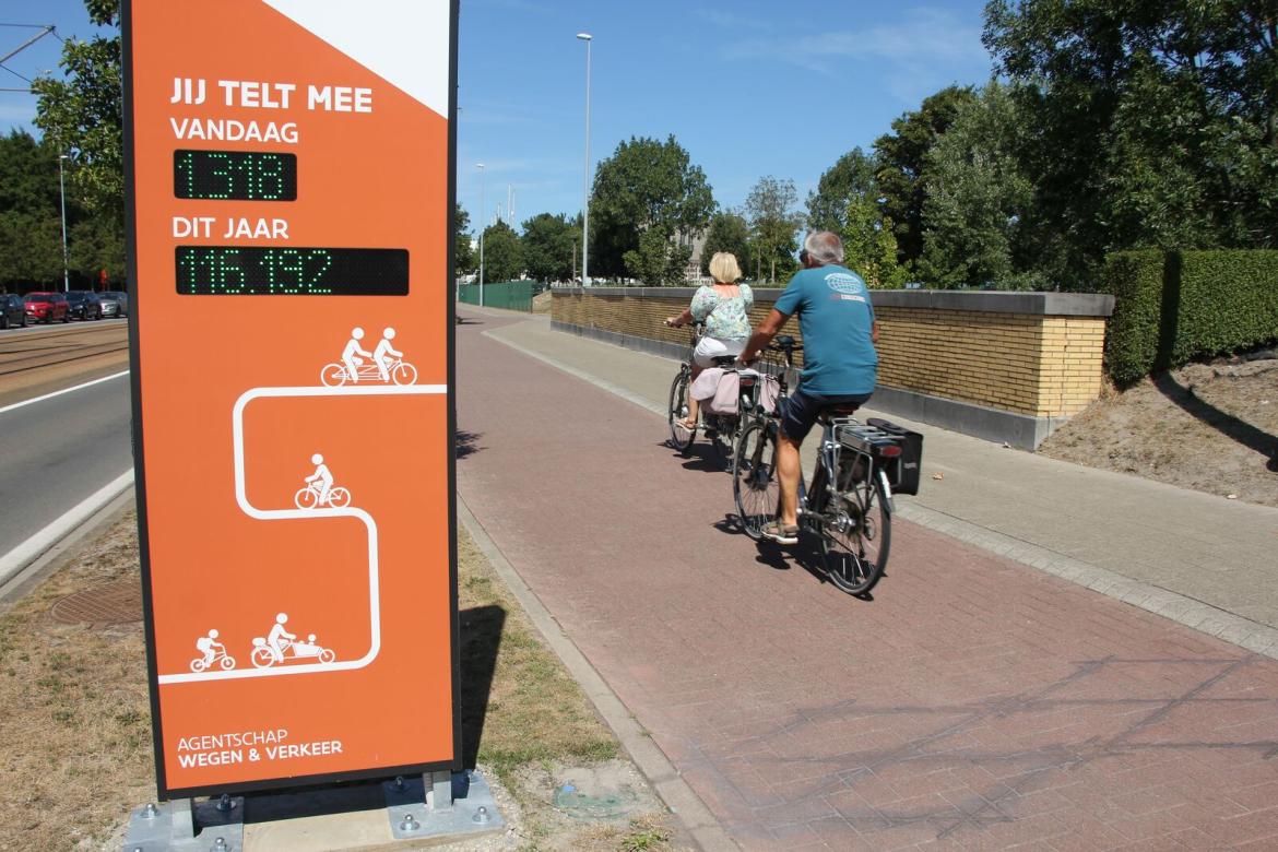 Fietsers rijden voorbij een fietstellerdisplay.