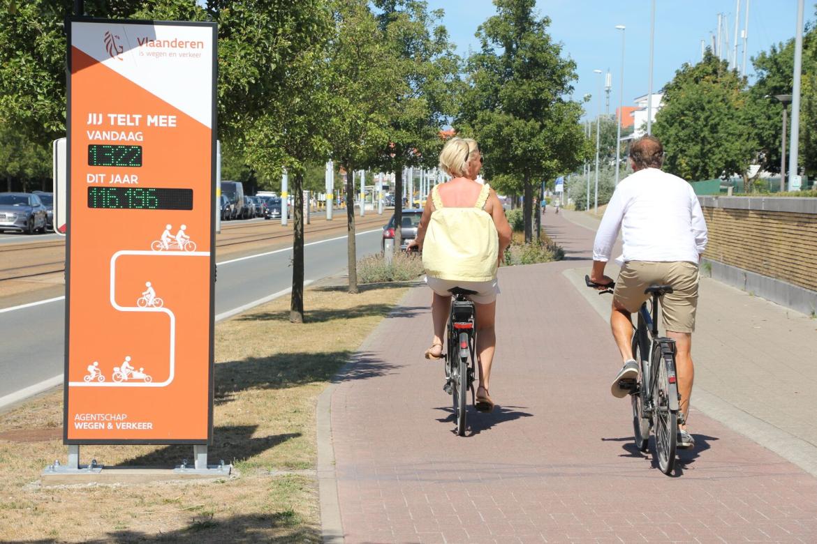 Twee zomerse fietsers rijden voorbij een fietsteller.